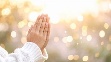 Imagem das mãos de uma mulher unidas em sinal de oração e em destaque luzes amarelas ao fundo, simbolizado a espiritualidade.