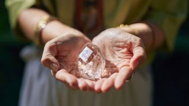 Imagem das mãos de uma mulher segurando uma pedra de cristal transparente, ofertando-a como um presente espiritual.