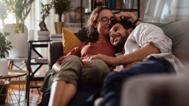 Imagem de um casal deitado em um sofá. Ambos estão felizes, conversando e se abraçando. A foto traz o conceito de alma gêmea.