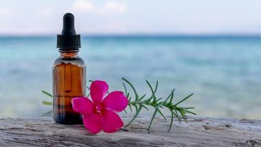 Imagem de um vidro conta gotas com óleo essencial e ao lado dele, uma flor rosa e um ramo de alecrim.