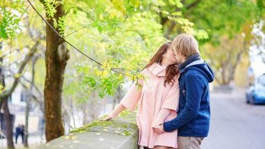 Imagem de um casal se beijando em uma rua, em frente a uma árvore durante o período de inverno.