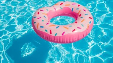 Imagem de uma piscina com água cristalina e sobre ela, uma boia de donuts na cor rosa.