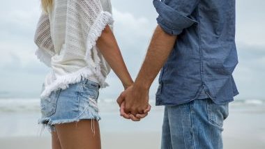 Imagem de um casal de namorados de mãos dadas, passeando na praia.
