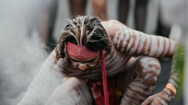 Imagem de um homem praticando um ritual. Seu corpo está todo pintado com listras na cor branca. A foto traz o conceito do Caboclo Tupinambá da Umbanda.