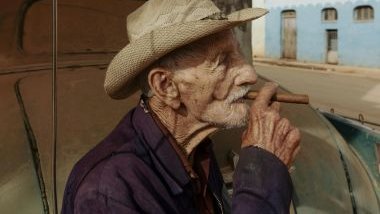 Imagem de um senhor usando um chapéu bege e fumando um cigarro de fumo de corda, simbolizando o Pai Maneco.