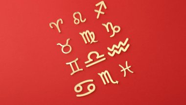 Os símbolos dos signos do zodíaco estão espalhados sobre uma superfície vermelha.