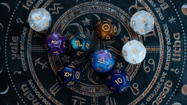 No foco da imagem, há uma Roda do Zodíaco com os símbolos dos signos e há dados em cima dela.