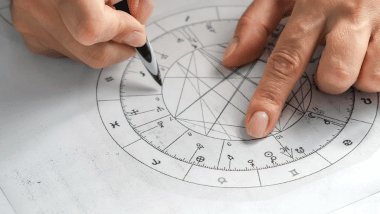 No foco da imagem, há uma Roda do Zodíaco desenhada em um papel com os símbolos dos signos.