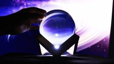 Há uma bola de cristal em destaque sobre um fundo roxo. A mão de uma pessoa toca na bola.