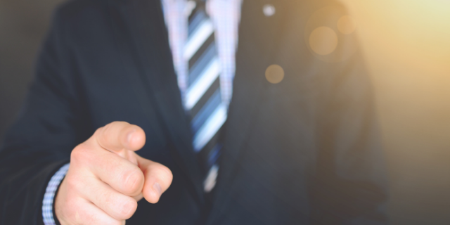 Homem vestido formalmente com o dedo indicador levantado.