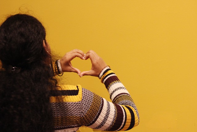 Mulher negra de costas fazendo coração com as mãos.