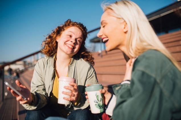 Duas amigas conversando sentadas enquanto riem 