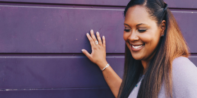 Mulher sorrindo com a mão apoiada na parede