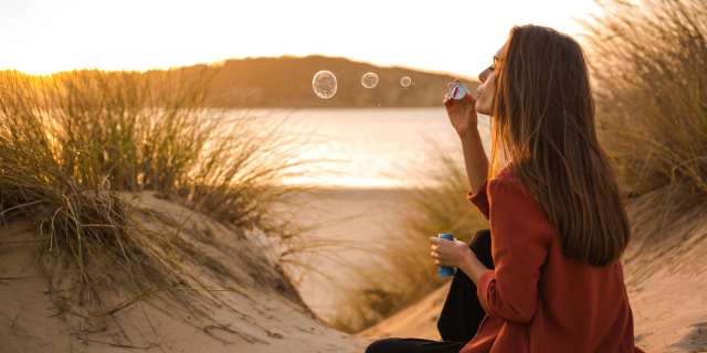 Mulher sentada na praia soprando bolinhas de sabão