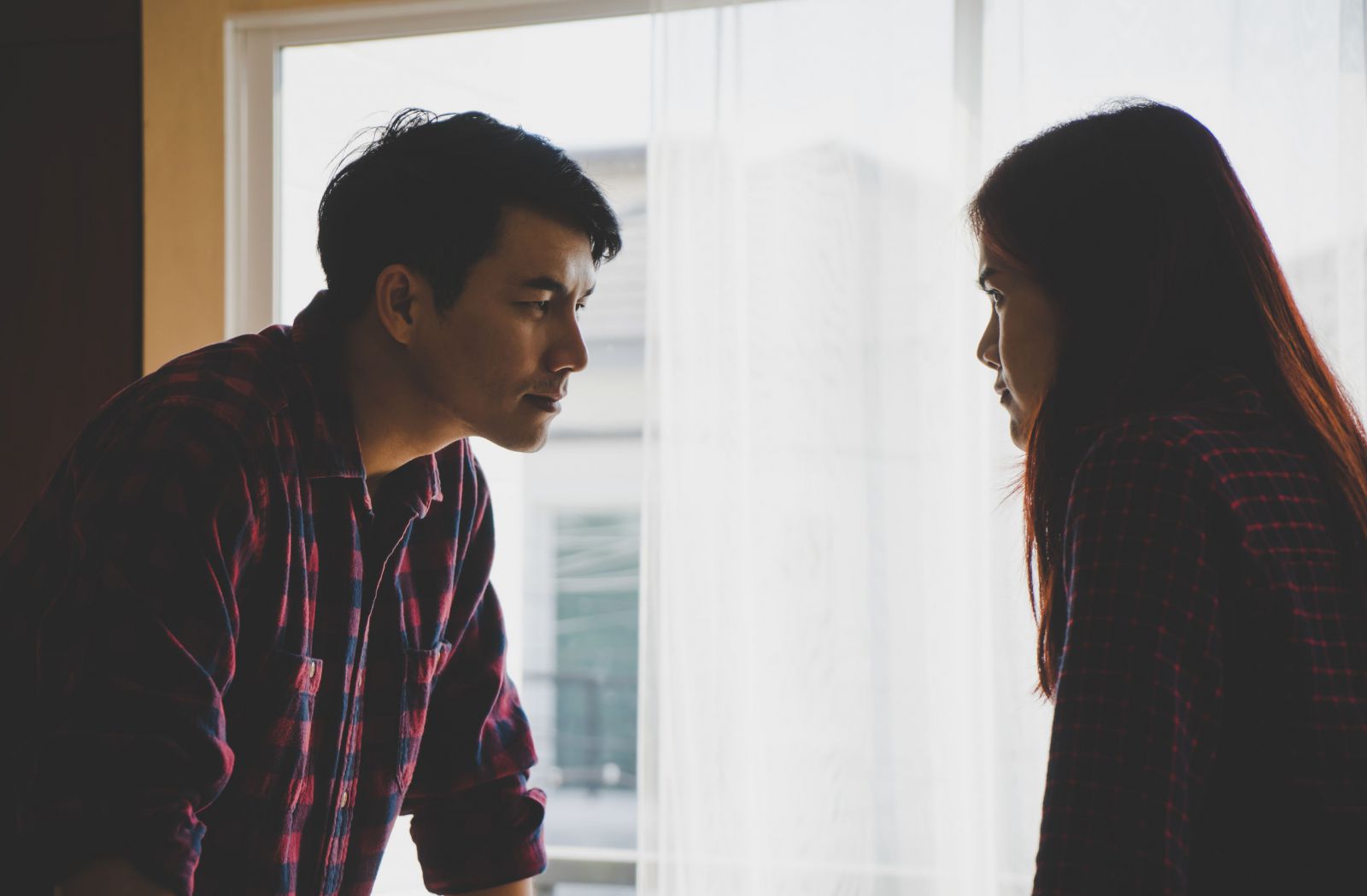 Homem e mulher olhando um para o outro ao lado de uma janela