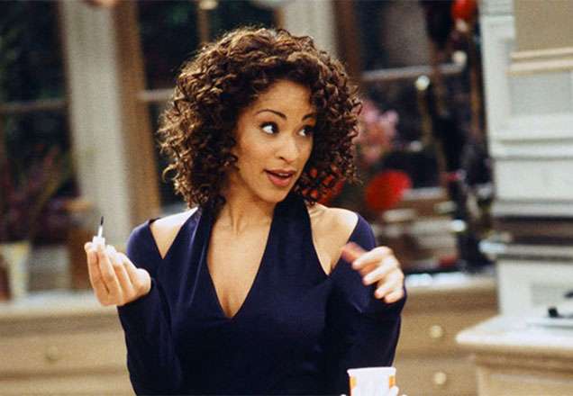 Mulher negra de pele clara, cabelos curtos e cacheados, usando blusa azul marinho.