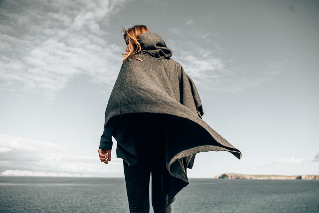 Mulher branca de costas com mar ao fundo.