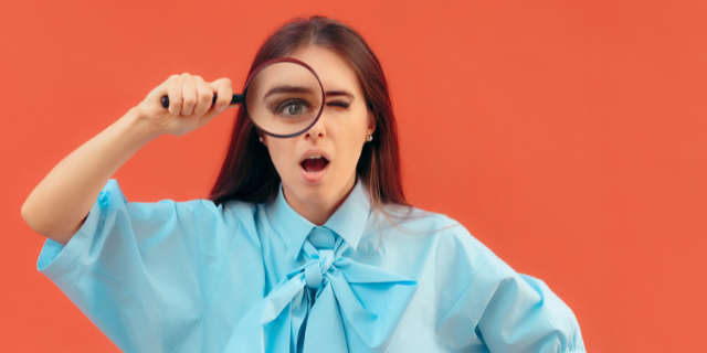 Mulher com cara de surpresa segurando uma lupa no rosto