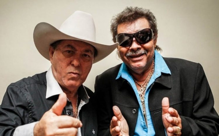 Milionário e José Rico olhando para frente sorrindo e fazendo gestos com a mão