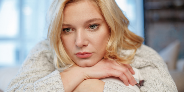 Mulher com os braços cruzados na mesa olhando triste