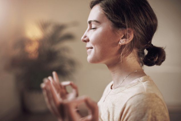 Mulher de olhos fechados fazendo sinal de meditação com as mãos