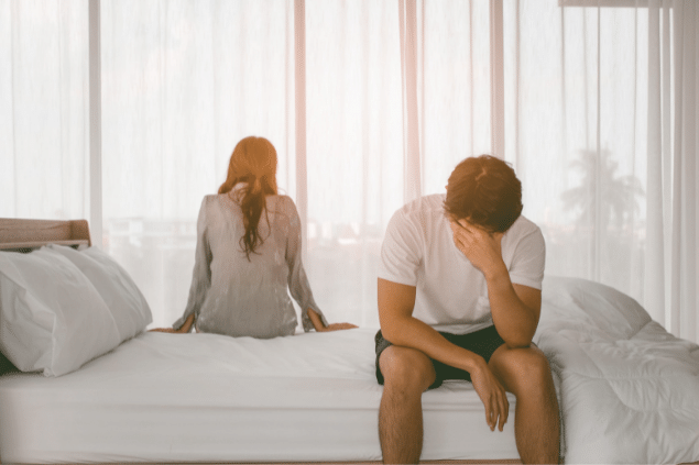 Casal sentado na cama de costas para o outro.