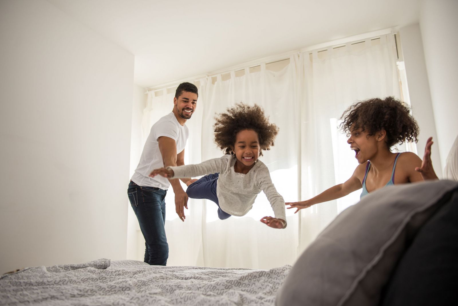 Criança pulando na cama com seus pais ao lado
