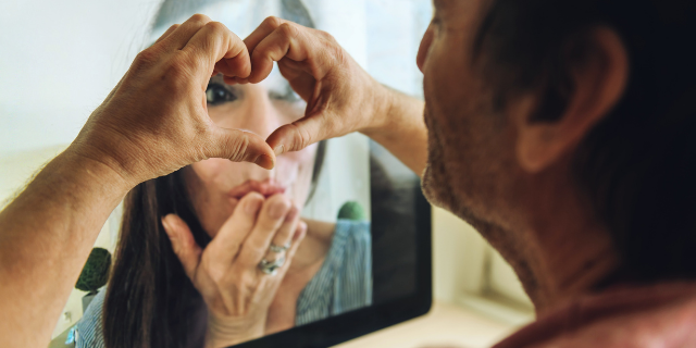 Casal fazendo uma videochamada e o homem fazendo um coração com as mãos