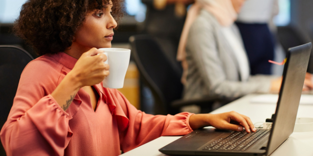 Mulher séria tomando café e trabalhando em um escritório