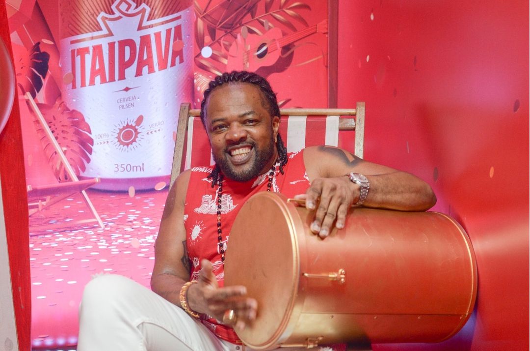 Homem negro sentado numa cadeira de praia, tocando tambor.