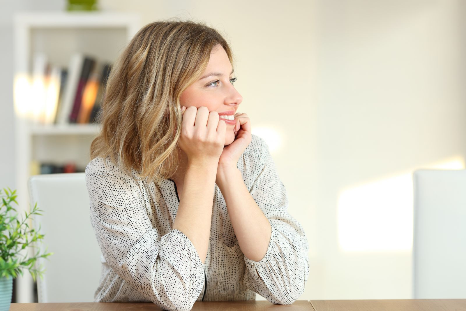 Mulher sorrindo olhando para o lado com as mãos no queixo