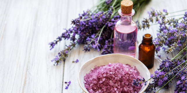 Lavanda em diferentes formatos sobre superfície de madeira branca. Há também dois frascos de vidro.