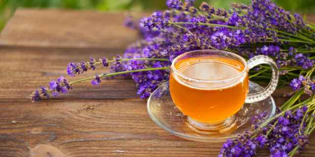 Xícara de chá em frente de lavanda. Ambos estão sobre superfície de madeira.