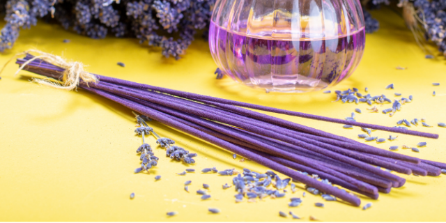 Incenso de cor roxa sobre superfície amarela. Ao fundo, há um frasco e plantas.