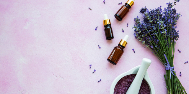 Lavanda em diferentes formas sobre um cenário roxo. Também há frascos de vidro marrom.