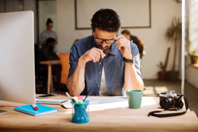 Homem concentrado enquanto olha para uma folha em branco em cima de uma mesa de trabalho