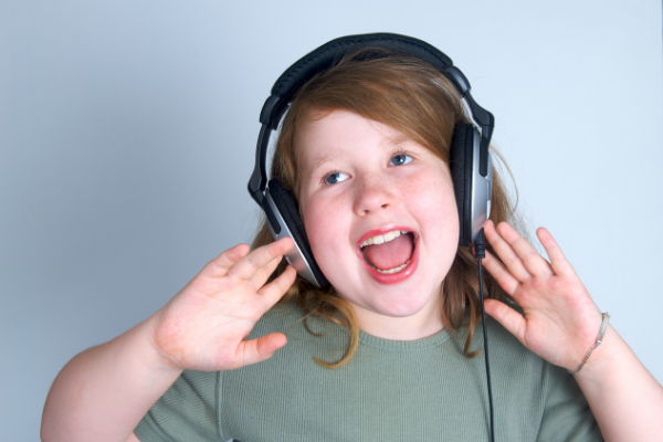 Menina cantando enquanto segura fones de ouvido