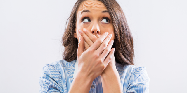 Mulher com o semblante surpreso coloca ambas as mãos sobre a boca.