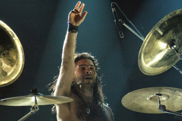 Ricardo Confessori de mão levantada em frente a bateria