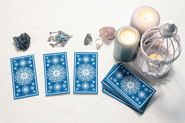 HappyNati / Getty Images / Canva Algumas cartas de Tarot viradas para baixo estão em destaque na imagem. Ao lado, há três velas e outros objetos.