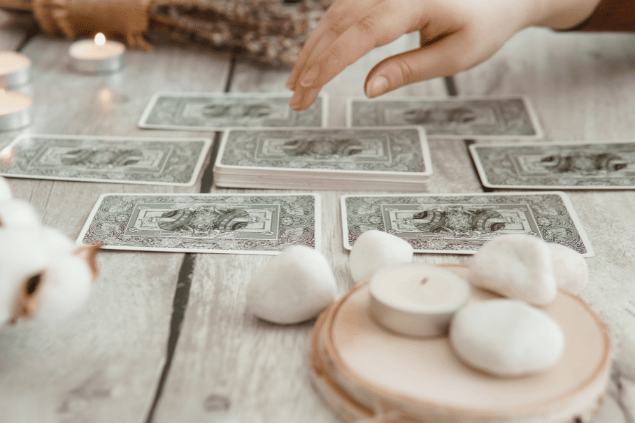 Algumas cartas de Tarot viradas para baixo estão em destaque na imagem. Ao lado, há velas e outros objetos.