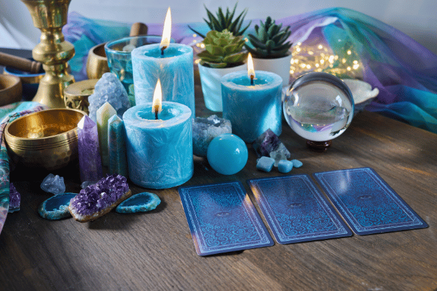 Algumas cartas de Tarot viradas para baixo estão em destaque na imagem. Ao lado, há velas e outros objetos.