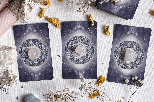 Algumas cartas de Tarot viradas para baixo estão em destaque na imagem. Ao lado, há flores e outros objetos.