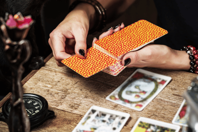 As mãos de uma taróloga segurando cartas de Tarot viradas para baixo estão em destaque na imagem.