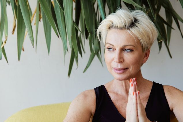 Foto de uma mulher com as mãos juntas, refletindo e sorrindo.