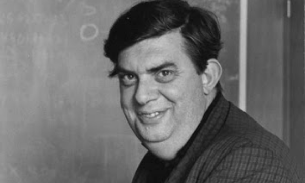 Geoffrey Ronald Burbidge sorrindo ao lado de uma lousa