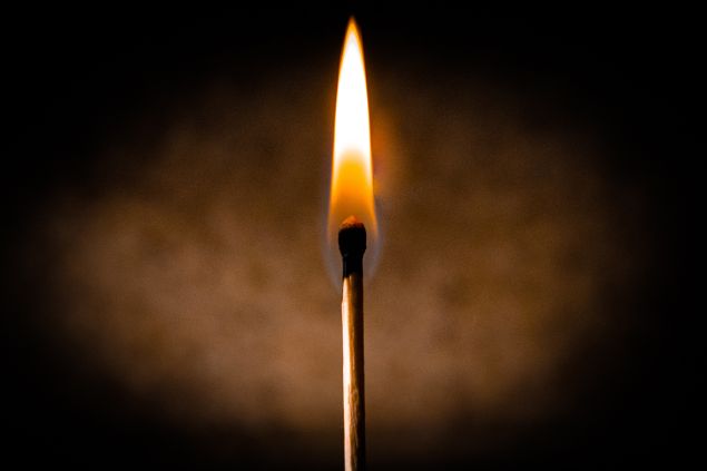 Imagem de um fósforo acesso em um fundo marrom