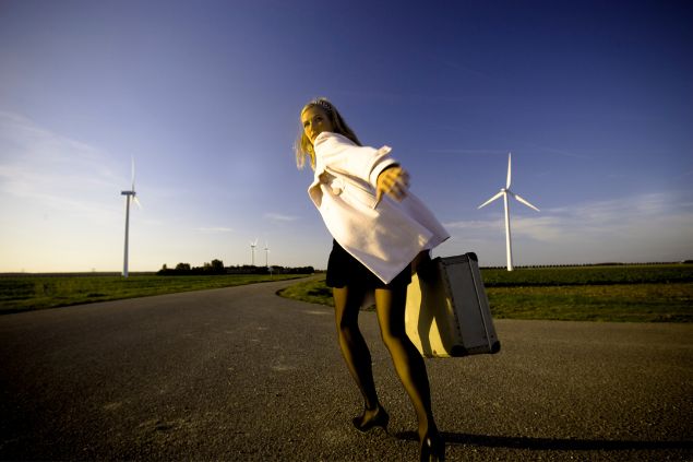 Imagem de uma mulher com uma mala na mão correndo e olhando para trás em uma estrada como se estivesse fugindo