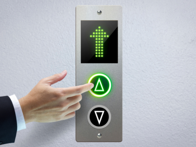 Pessoa apertando botão de elevador e visor mostrando seta para cima