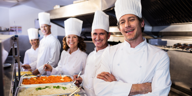 Cinco chefs de cozinha sorriem em cozinha. 